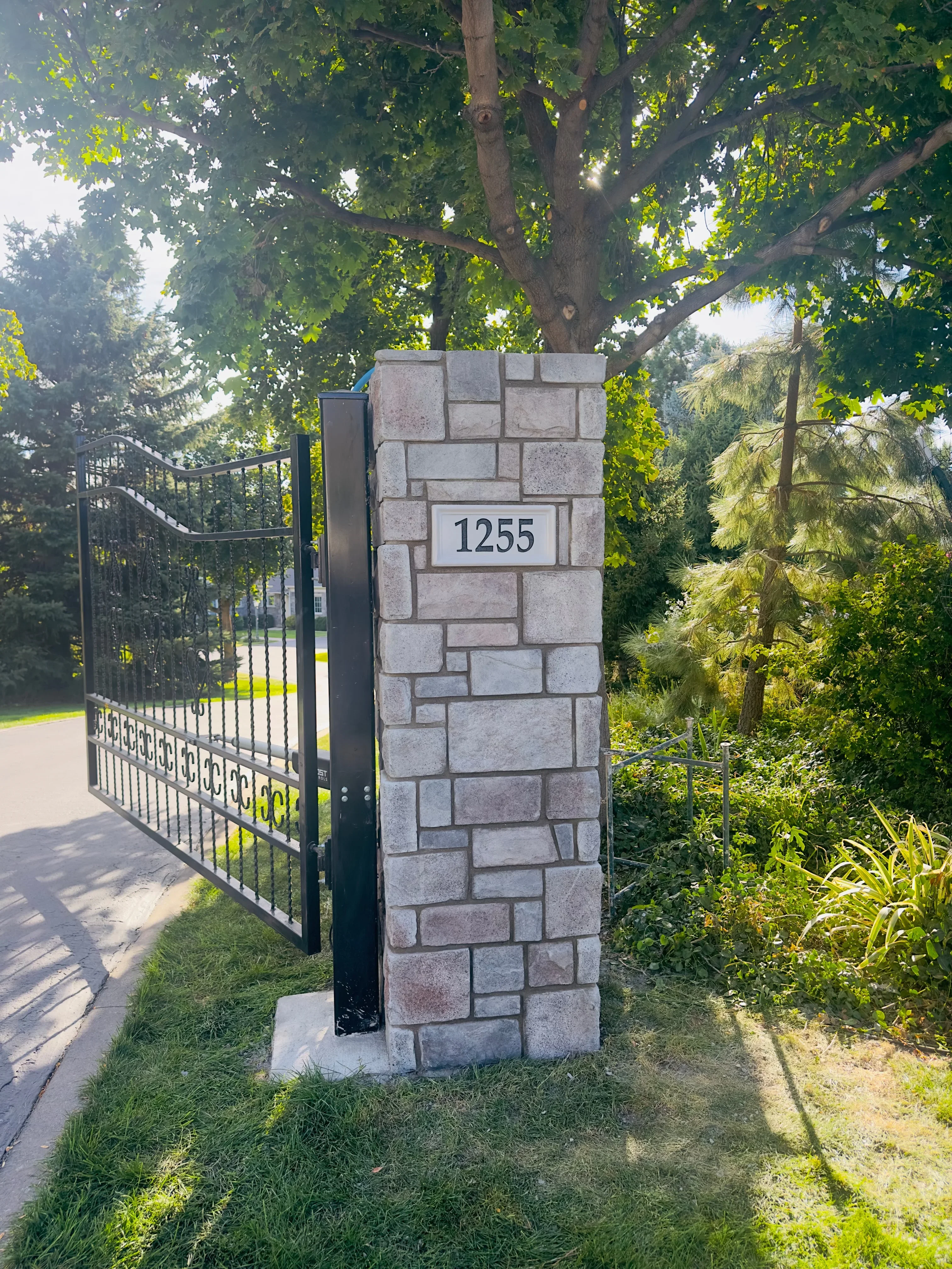 Light gray stone masonry pillar with address plaque and black metal gate attachment