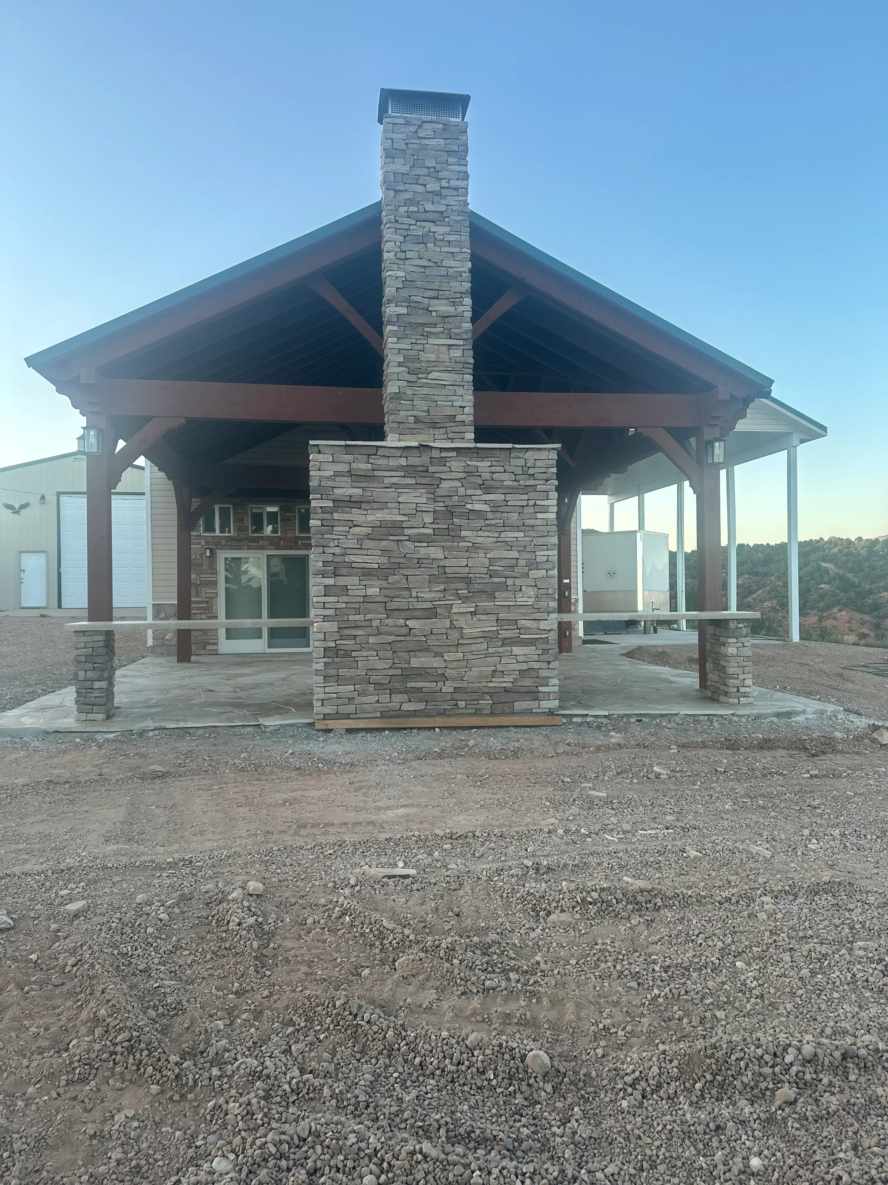 Stacked stone chimney with metal cap on concrete patio under covered timber frame structure
