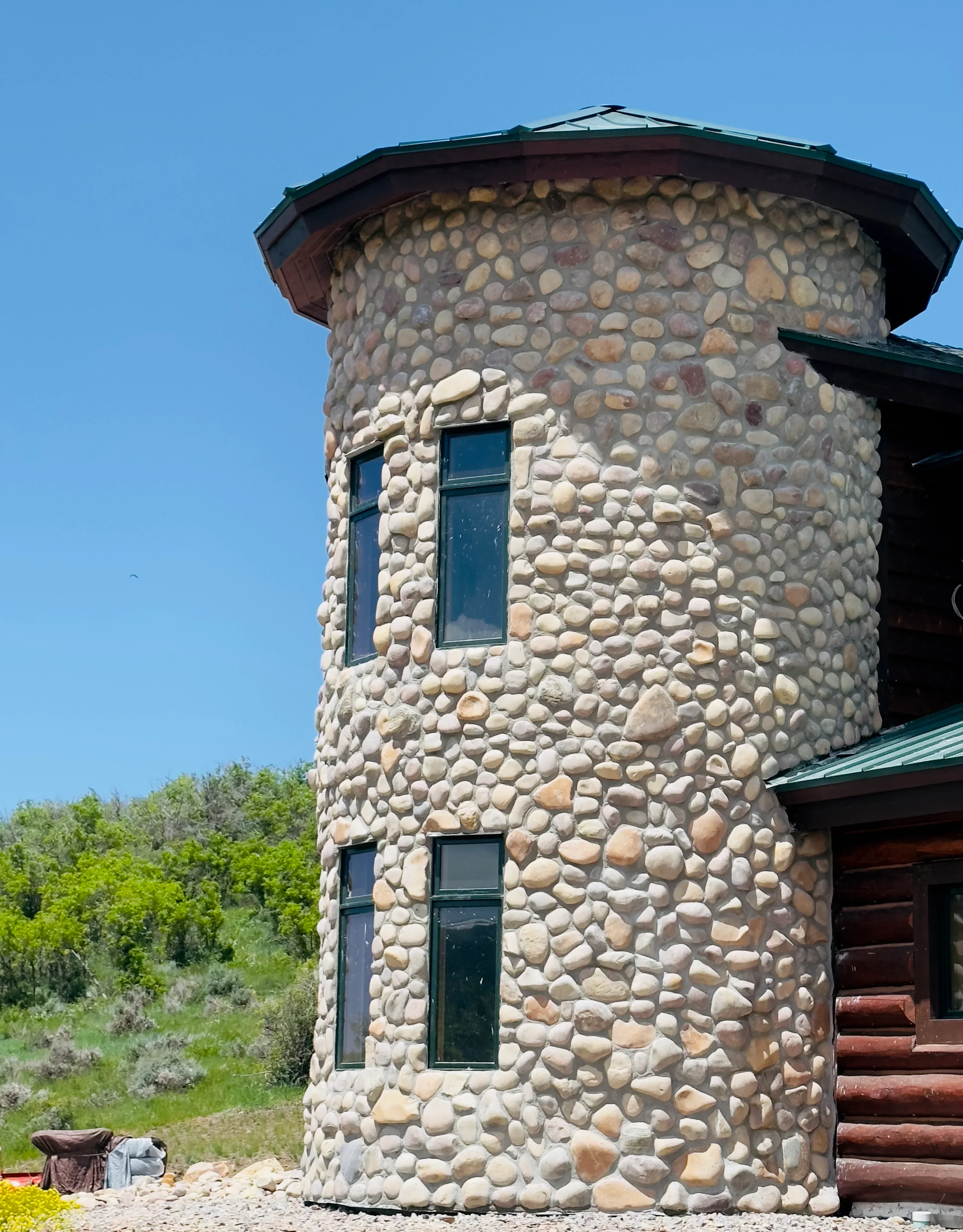 Round stone tower with hand-laid fieldstone masonry, two windows, and green metal roof cap