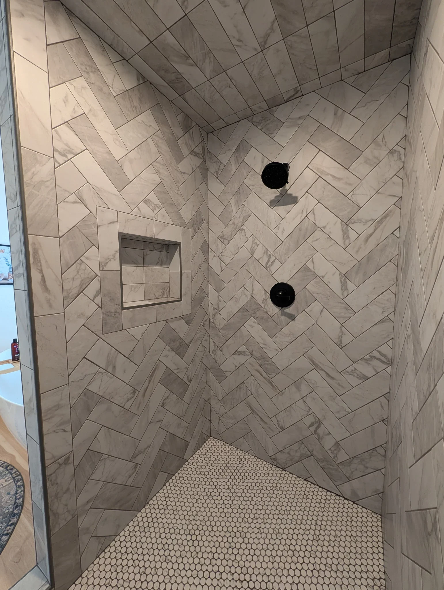 Marble herringbone tile shower walls with penny tile floor and recessed niche