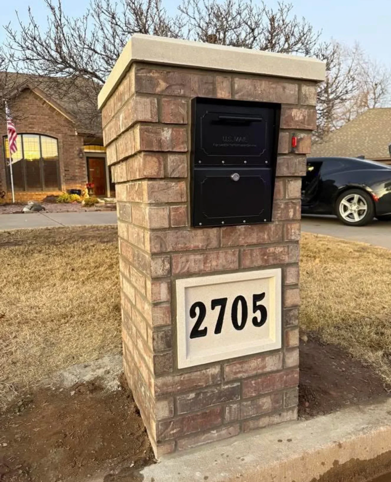Red brick mailbox post with concrete cap, black metal mailbox, and address plaque