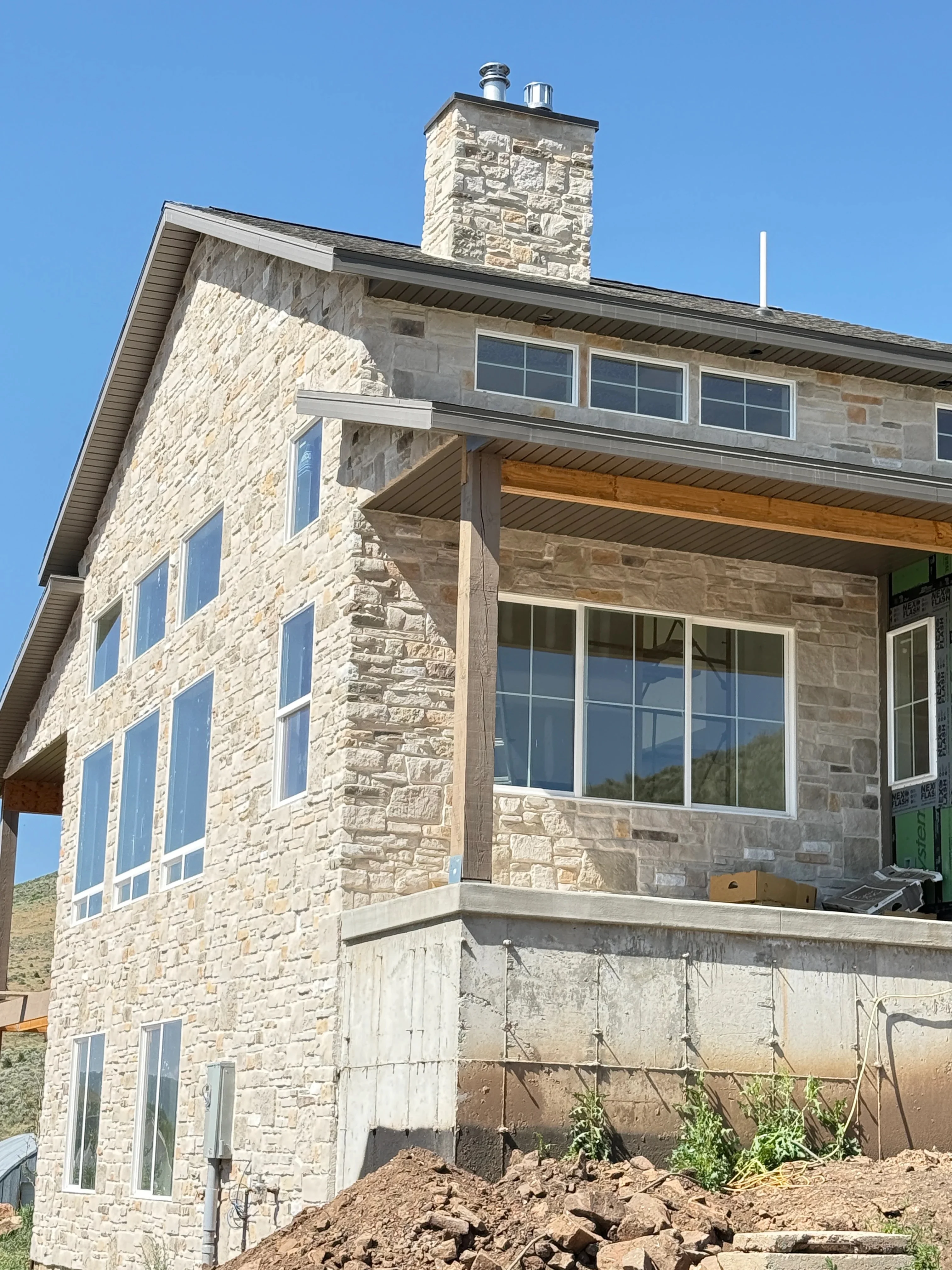 Cut stone veneer masonry exterior with mortar joints, multi-pane windows, and metal chimney