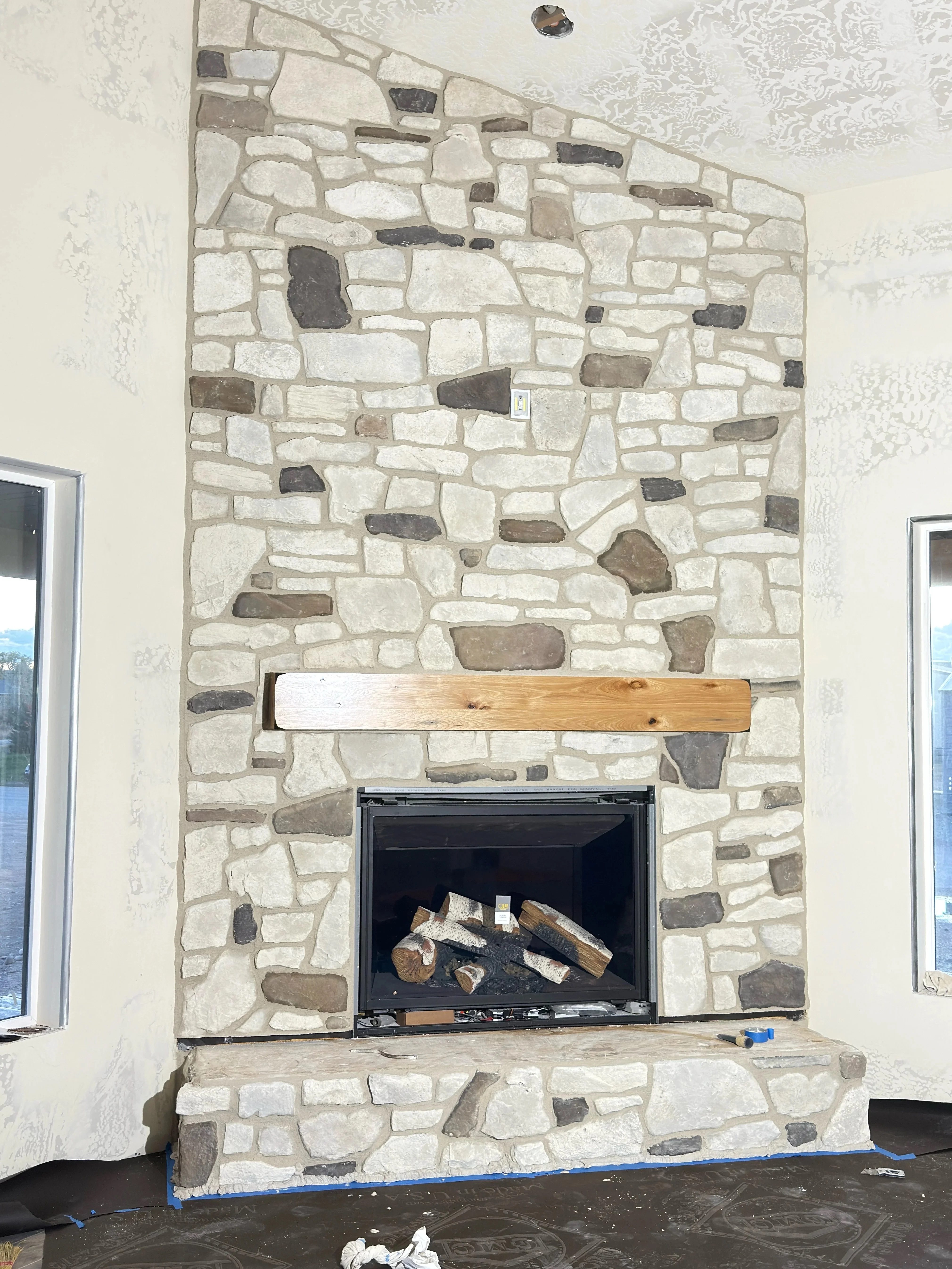 Multi-colored natural stone fireplace with random ashlar pattern, black firebox insert, and wood mantel beam