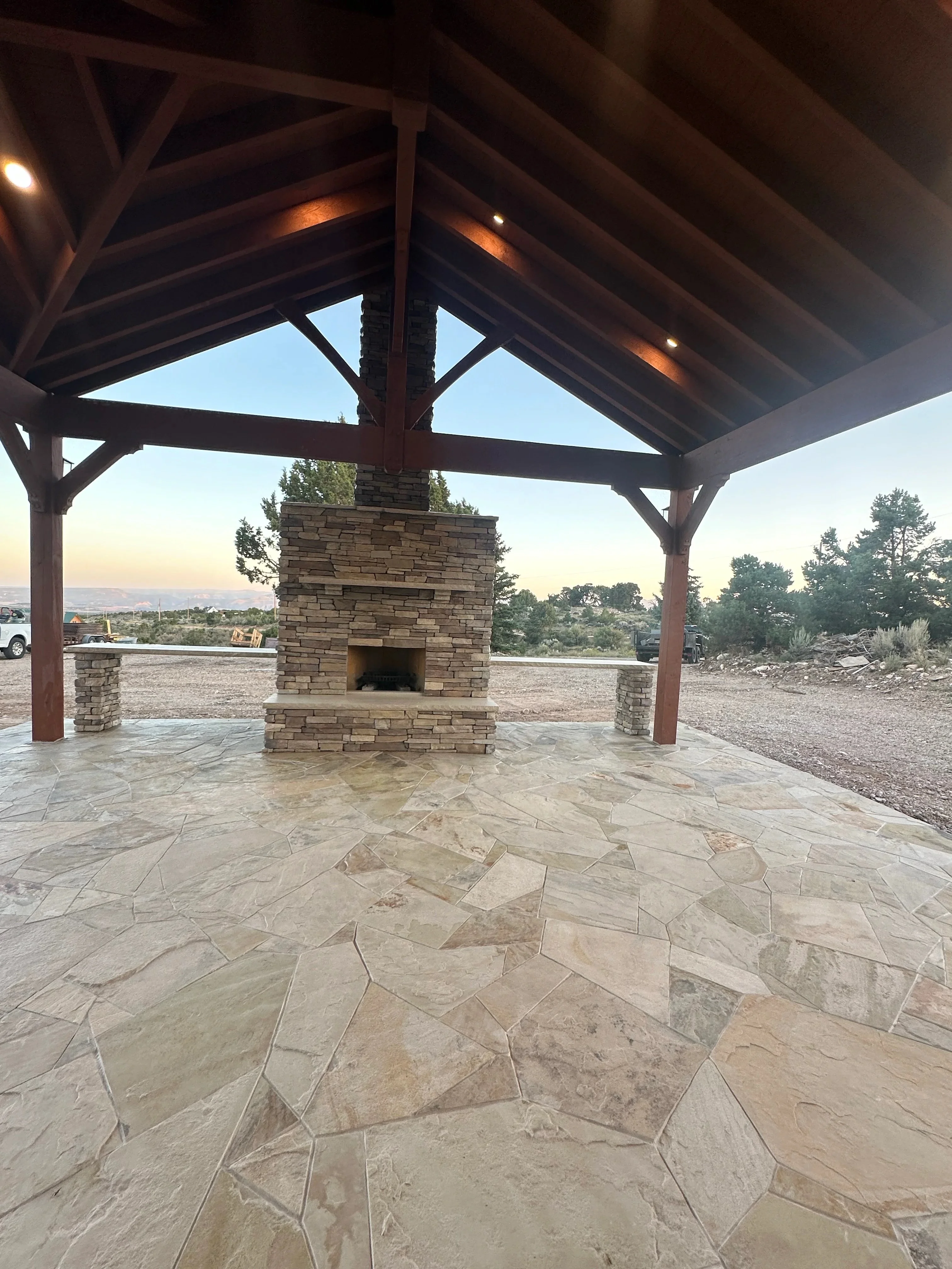 Stacked stone fireplace with timber pavilion, flagstone patio, and stone veneer pillars