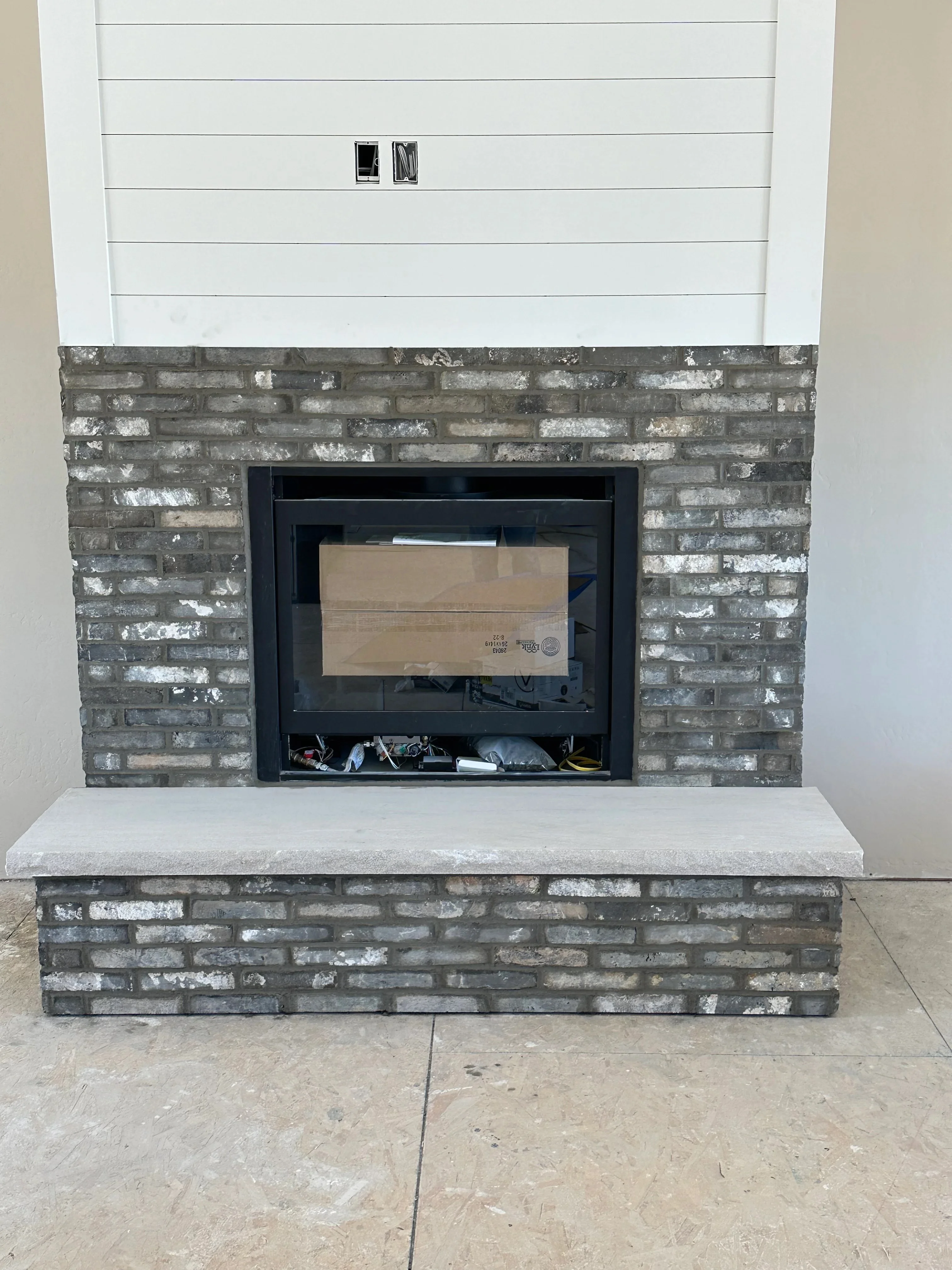 Gray and tan brick veneer fireplace surround with concrete hearth and black steel insert frame