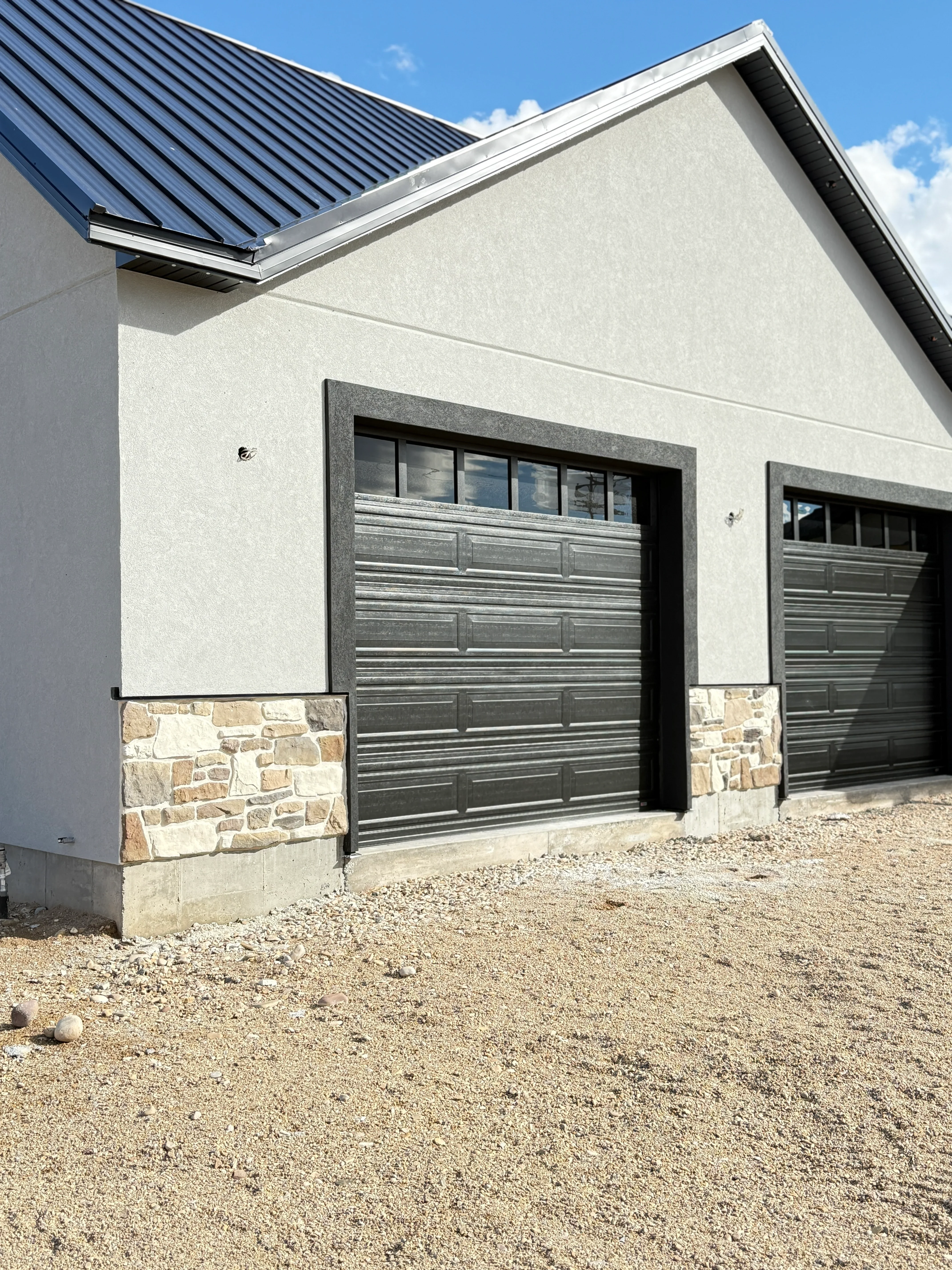 Stacked stone veneer garage base with white stucco walls and metal roof