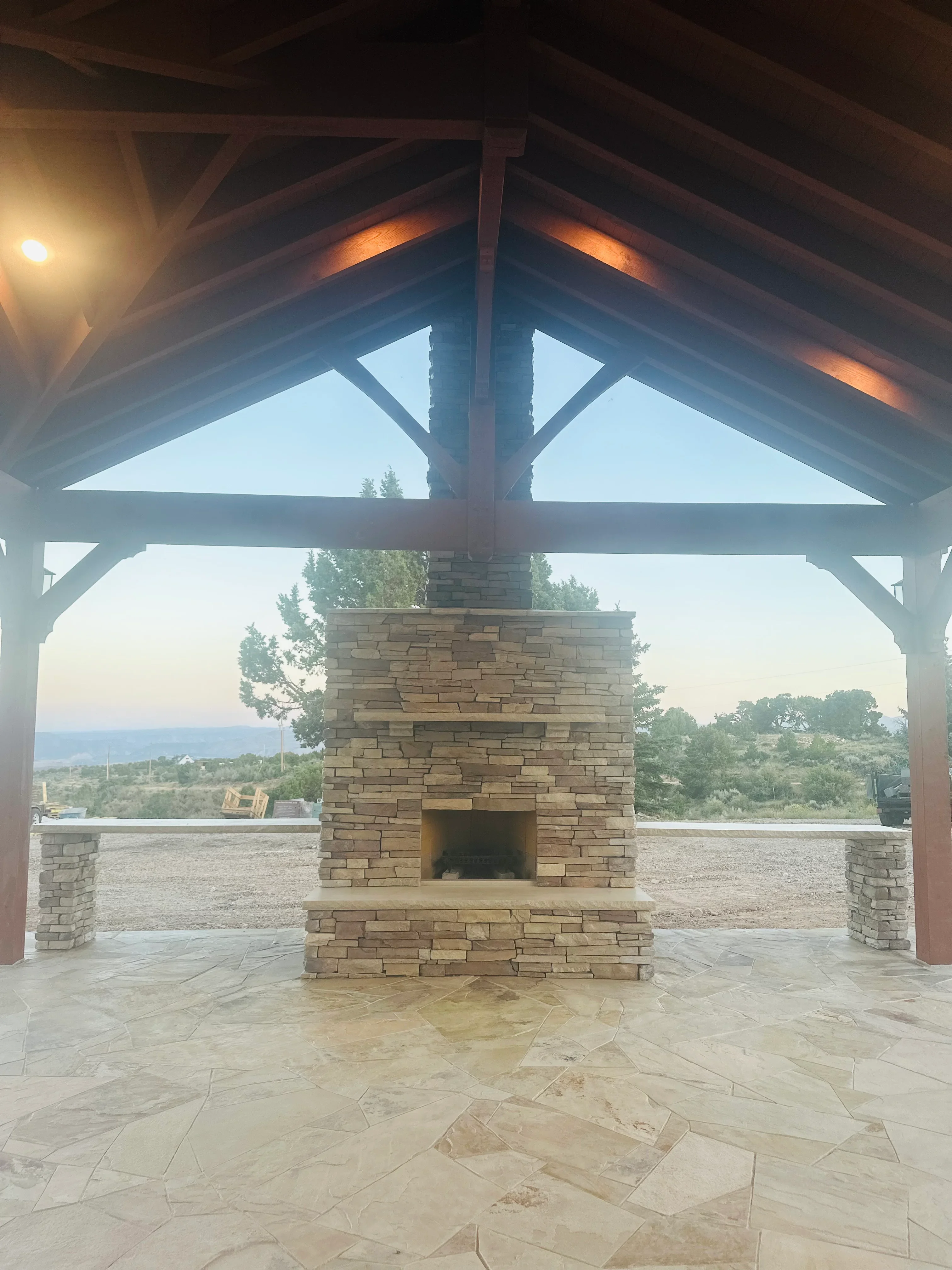 Stacked stone brick fireplace with hearth under timber pergola with decorative bracing
