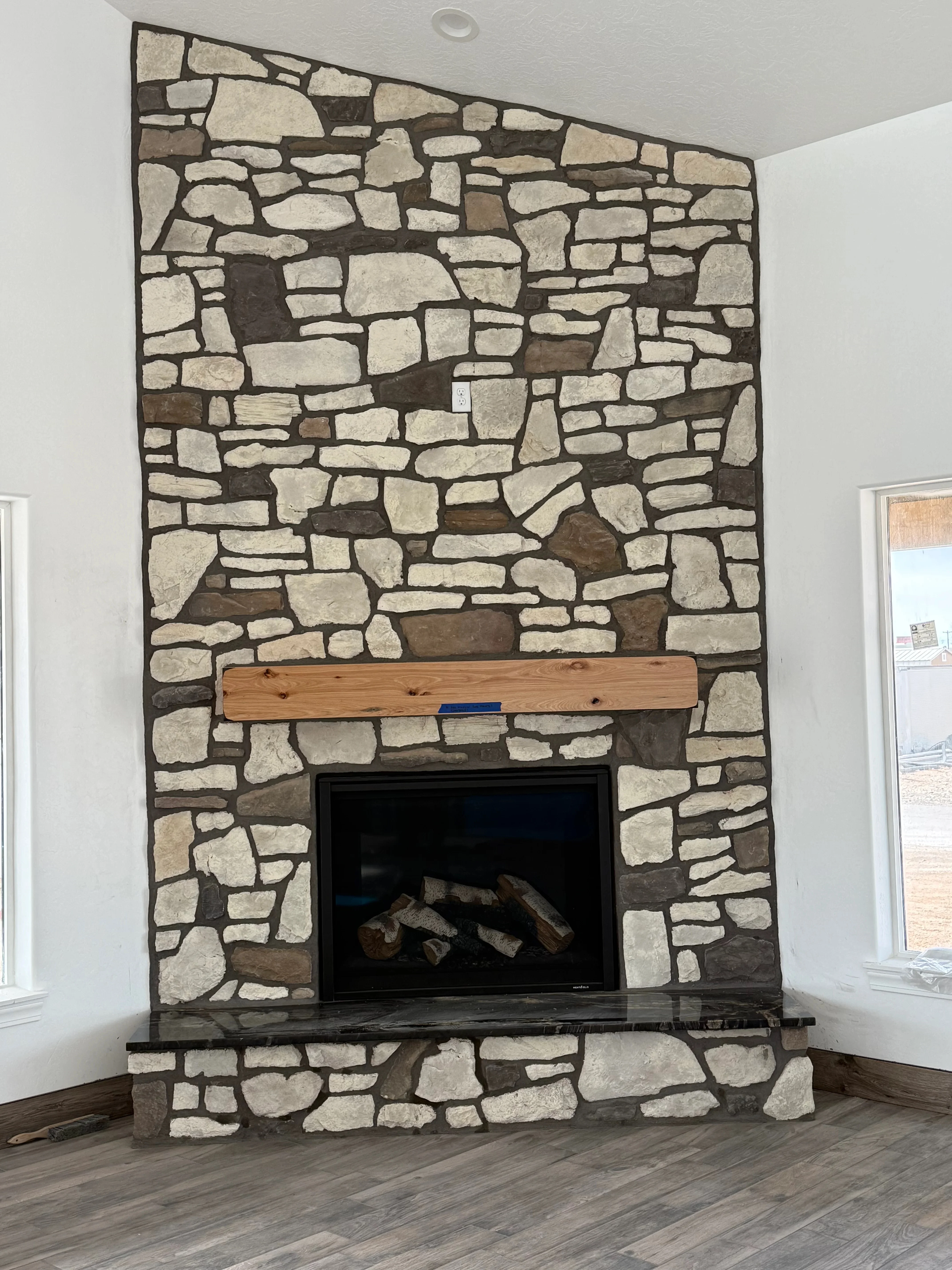Mixed tan and brown cut stone fireplace with black firebox and wood mantel